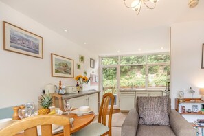 A dining area with a table set for two, a sofa, and a window with a view of greenery. - 2 Bed in Nolton Haven (oc-fb098) (Nolton Haven)