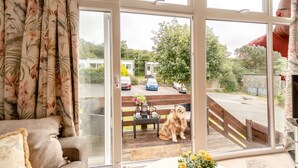 Ein Zimmer mit einer großen Schiebeglastür, die auf eine Terrass mit Hund, Bank und einem Tisch mit Blumenvase führt.
