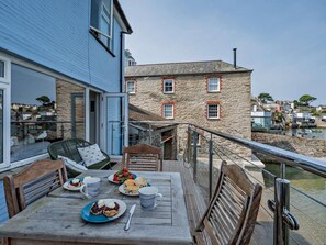 Un comedor con una mesa dispuesta para dos, con vista a un edificio de piedra y un cuerpo de agua.