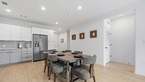 A modern kitchen with white cabinets, a stainless steel refrigerator, and a dining table with chairs. - 2BR South Congress Condo for 6, Near DT! (Austin)