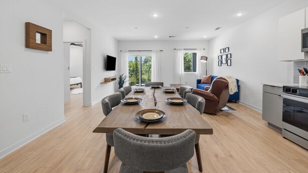 A modern dining area with a wooden table, grey upholstered chairs, and a kitchen area with a built-in oven and microwave. - 2BR South Congress Condo for 6, Near DT! (Austin)