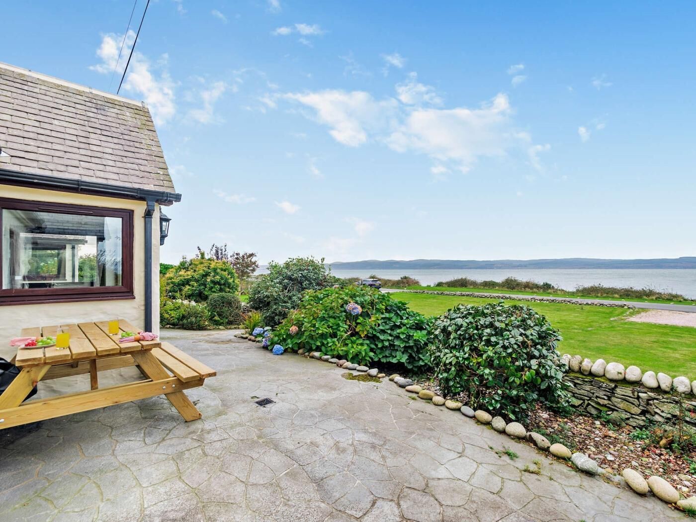A patio with a wooden table and chairs, a stone pathway, and a view of the sea.