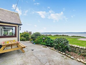Eine Terrasse mit einem Holztisch und -stühlen, einem gepflasterten Weg und Blick aufs Meer.