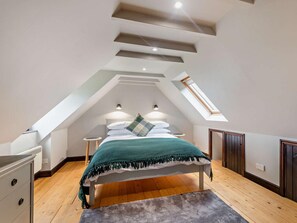 Ein Schlafzimmer mit schrägen Wänden, einem Bett mit grüner Decke, zwei Nachttischen und einem Dachfenster.