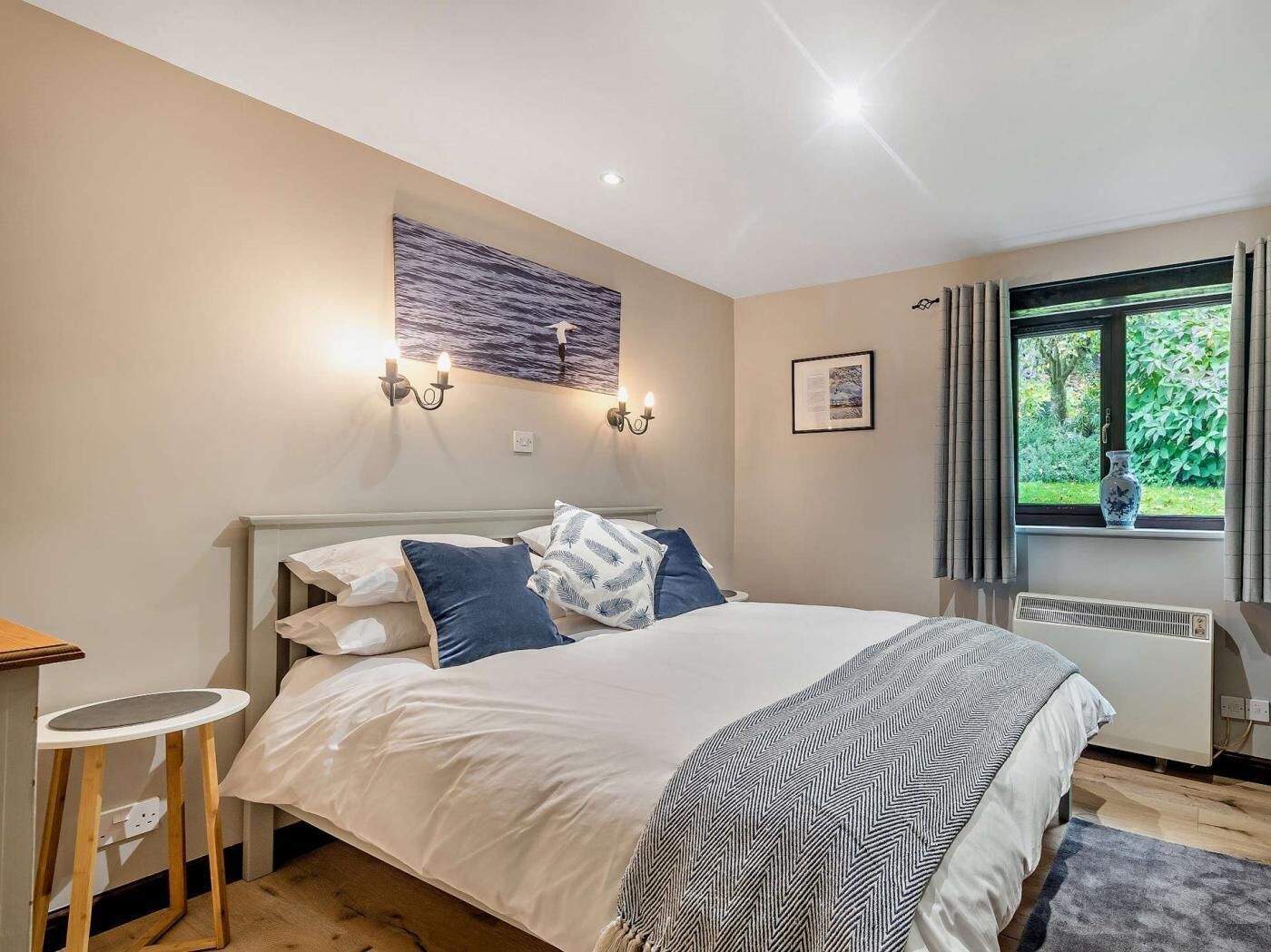 A bedroom with a bed, bedside table, wall art, window, and a radiator.