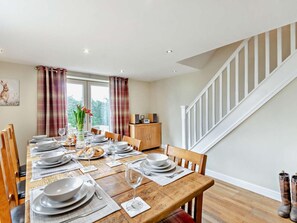 A dining area with a wooden table set for six, a wooden cabinet, and a staircase. - 4 Bed in Matlock (oc-93830) (Crich)
