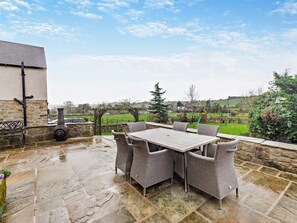 An outdoor patio with a stone floor, a table, and wicker chairs. - 4 Bed in Matlock (oc-93830) (Crich)