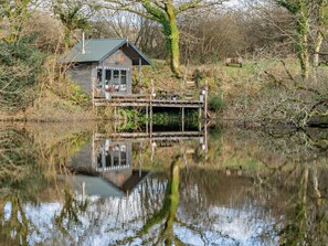A wooden cabin with a dock extending into a calm lake, surrounded by trees and vegetation. - 3 Bed in Swansea (oc-93942) (Southgate)