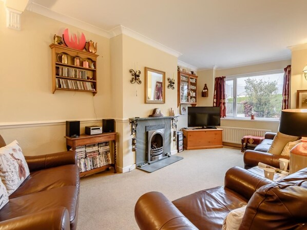 A living room with a fireplace, a television, leather sofas, a bookshelf, and a window with curtains. - 3 Bed in Keswick (oc-93949) (Portinscale)