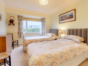 A bedroom with two beds, a dresser, a chair, a window with curtains, a lamp, and a framed picture on the wall. - 3 Bed in Keswick (oc-93949) (Portinscale)