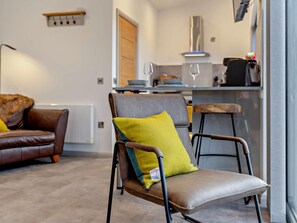 A modern living room with a leather sofa, a brown chair with a yellow cushion, and a dining area with a bar and kitchen in the background.
