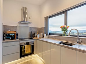 A modern kitchen with a built-in oven, a stainless steel range hood, a large window with a view, and a vase with flowers on the counter.