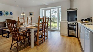 Eine moderne Küche mit Einbauofen, ein Essbereich mit Holztischen und -stühlen sowie eine große Schiebeglasdoor, die zu einem Garten führt.