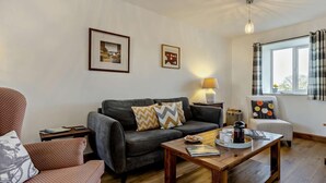 Ein Wohnzimmer mit einer Couch, Sesseln, einem Couchtisch und einem Fenster mit Vorhängen.