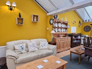 Ein Zimmer mit gelber Wand, einem beigen Sofa, einem Holzschrank und einem Esstisch.