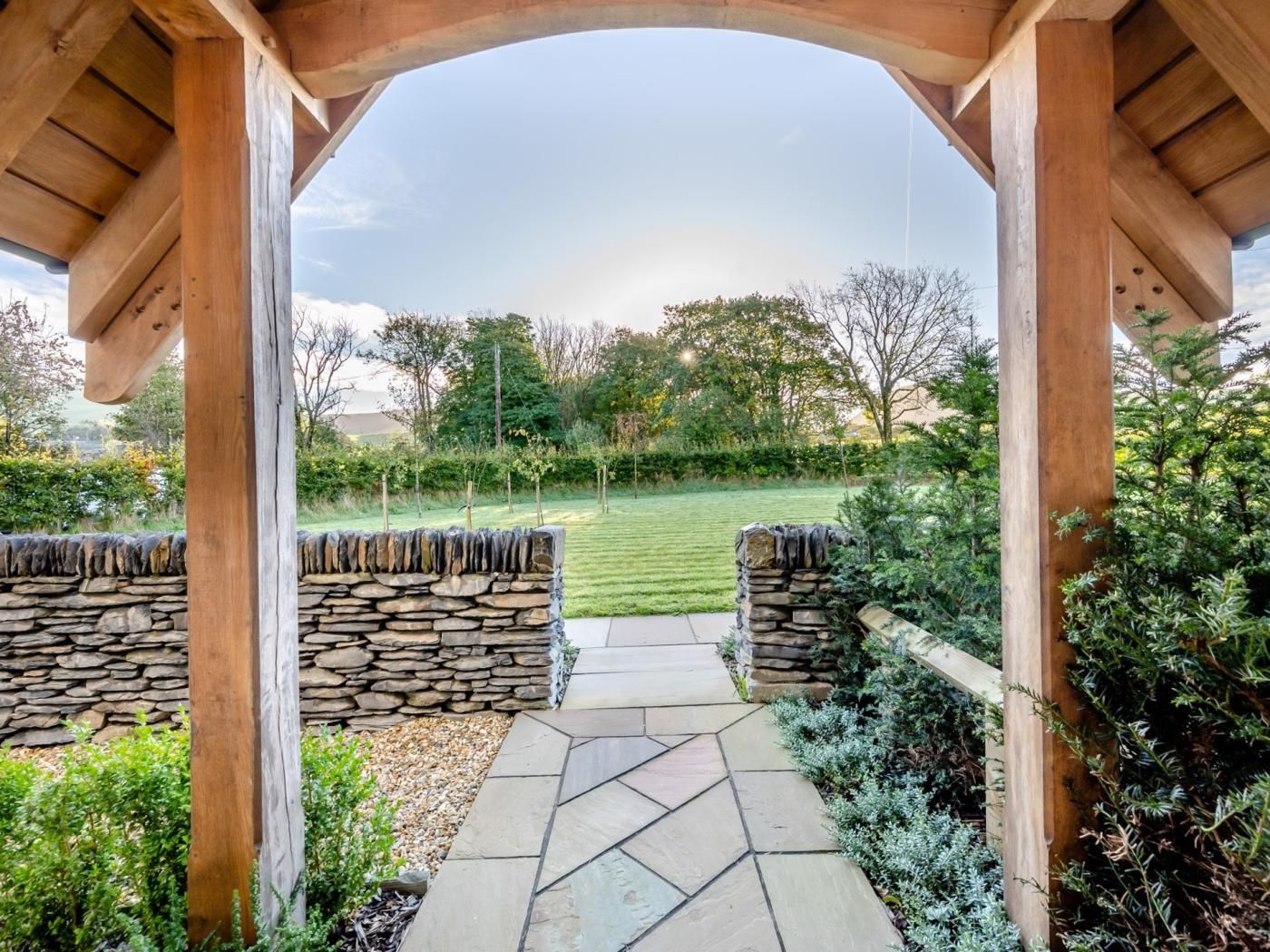 A stone pathway leading to a wooden pergola with a view of a well-maintained lawn and trees.