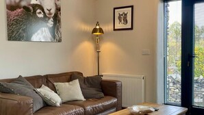 A living room with a brown leather sofa, a wooden coffee table, a floor lamp, and a door leading outside. - 1 Bed in Penrith (oc-94068) (Ullswater)