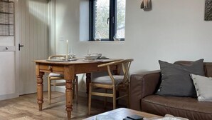 A cozy living room with a wooden dining table, a brown leather sofa, and a window with blinds. - 1 Bed in Penrith (oc-94068) (Ullswater)