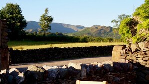 A stone wall with a wooden bench, a paved area, and a road leading to a mountainous landscape. - 1 Bed in Penrith (oc-94068) (Ullswater)