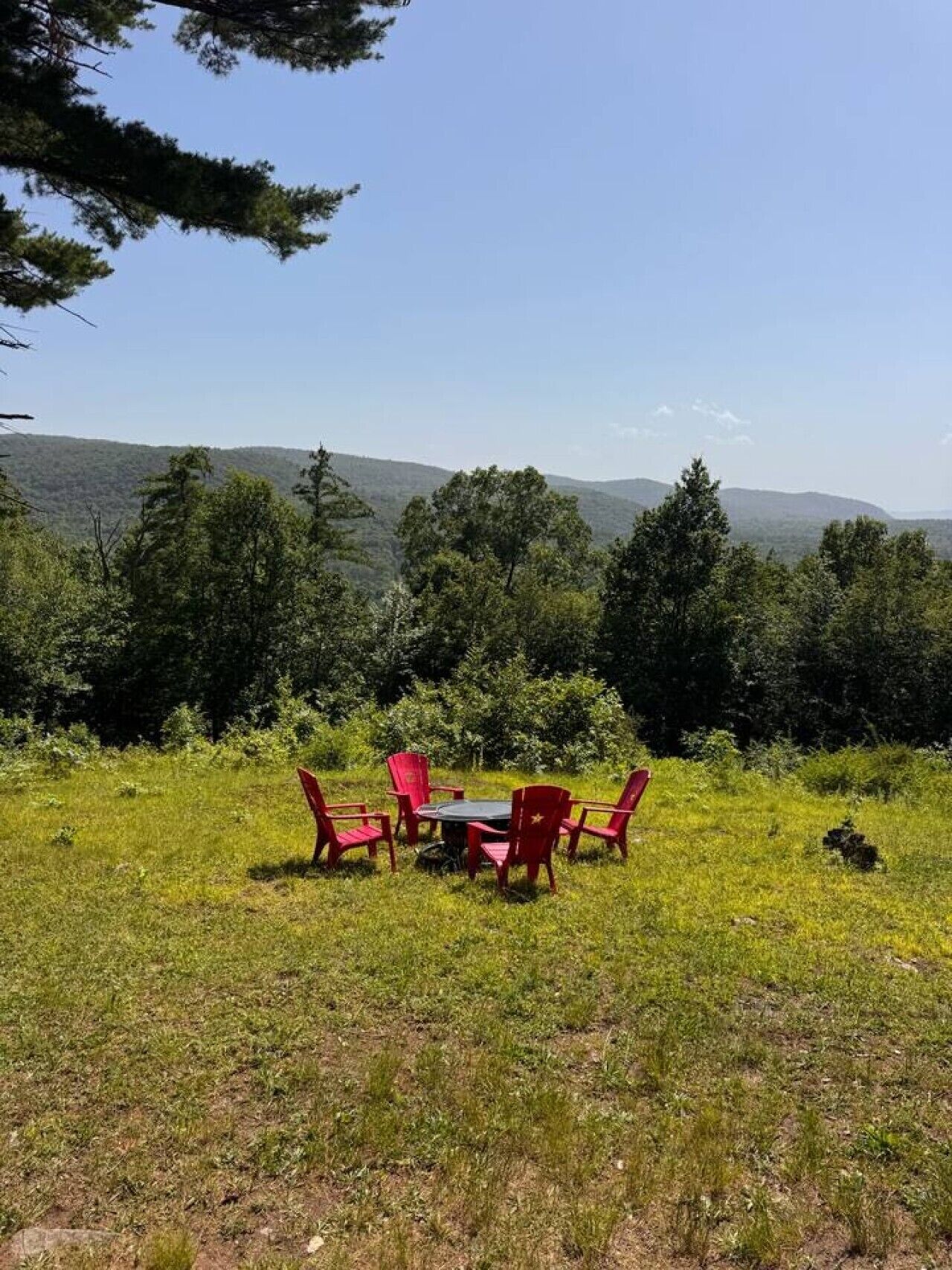 An outdoor seating area with a table and chairs, surrounded by grass and trees, with a view of distant hills.