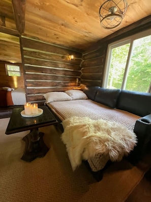 A cozy cabin interior with a wooden log wall, a sofa, a table with candles, and a window with a view of greenery. - Cozy Rustic Cabin with Scenic Views (Johnsonville)