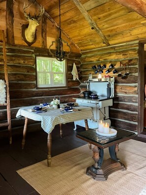 Interior rústic d'una cabana amb una taula de dinar, una estufa i un corró de cervís penjat.