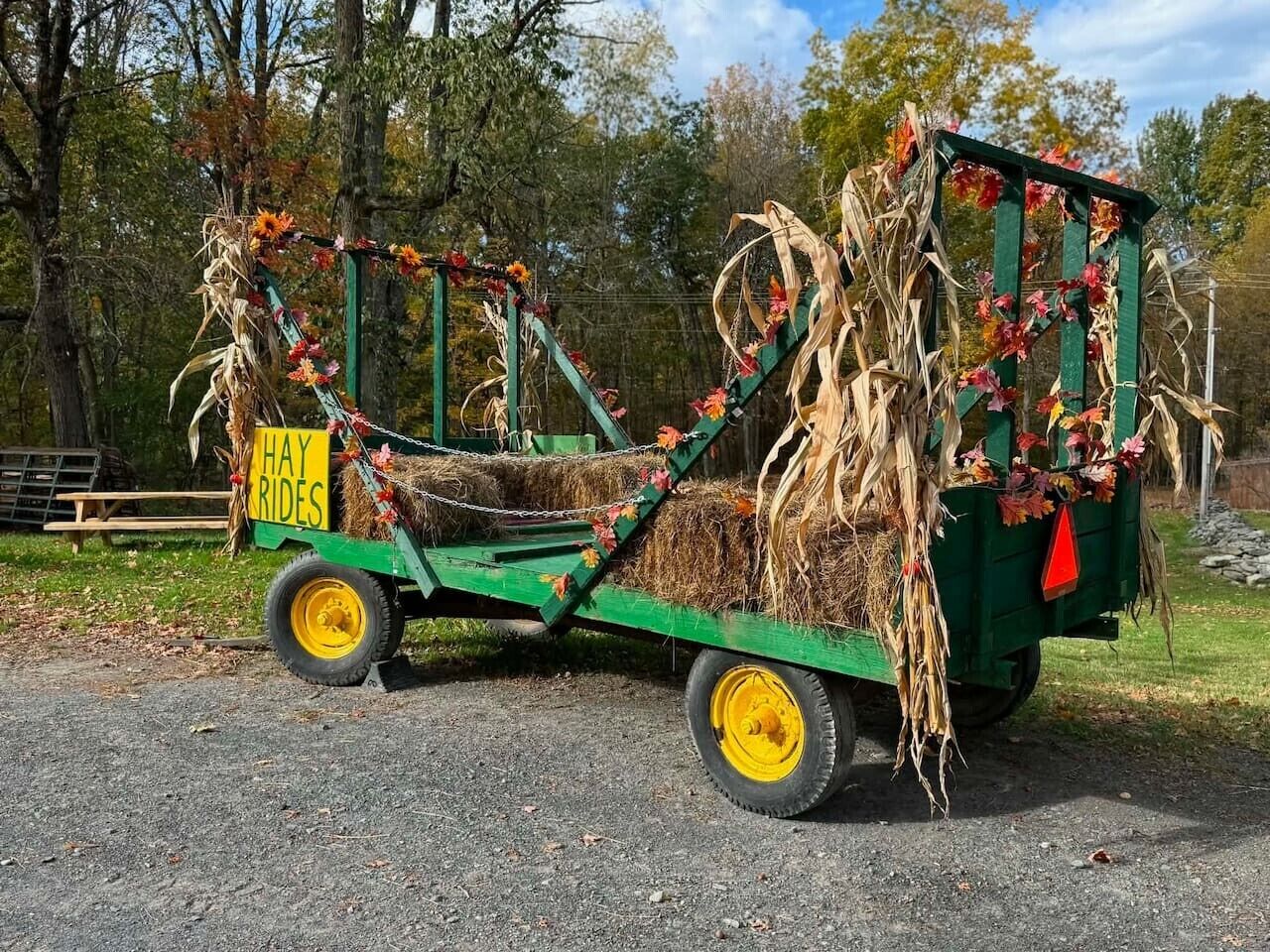 A green hay cart with 'HAY RIDES' signage, decorated with autumn leaves and corn stalks.
