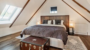 Ein Schlafzimmer mit schrägverdachter Decke, einem großen Bett, einer Kommode, einem Fenster und einer Heizung.