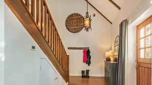 Eine Holztreppe, ein Kleiderständer mit Jacken, ein an der Wand befestigter Laternenleuchter und eine Tür mit Fenster.