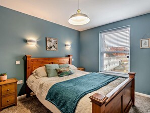 Ein Schlafzimmer mit einem hölzernen Bett, einem Nachttisch, einer Wandlampe und einem Fenster mit Jalousien.