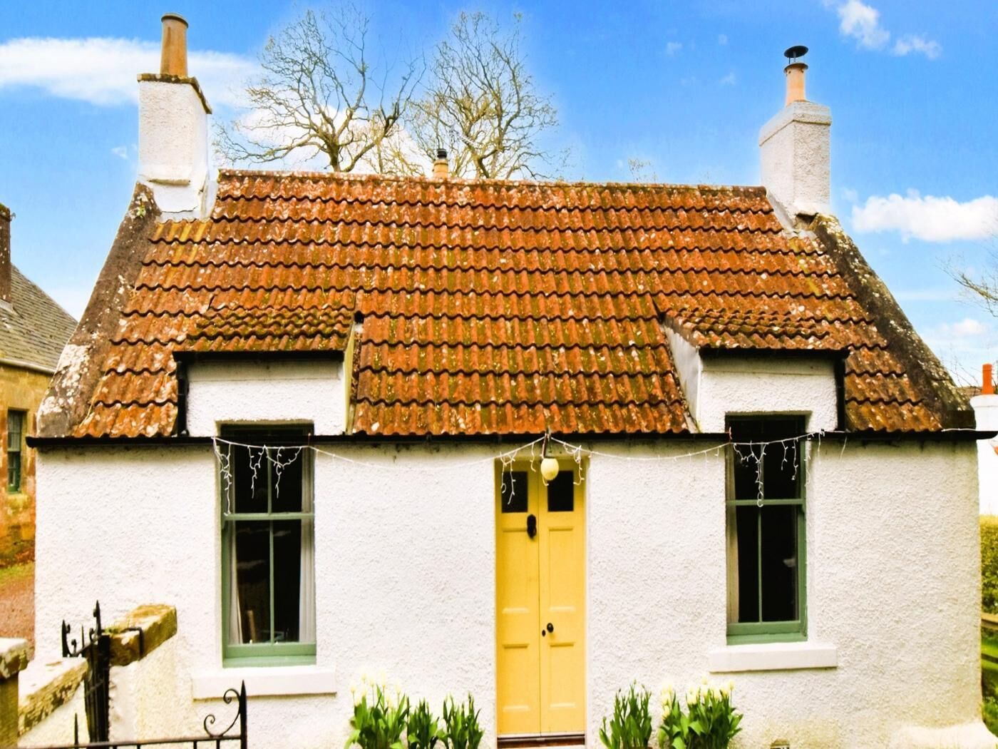A white building with a tiled roof, two chimneys, and a yellow door.