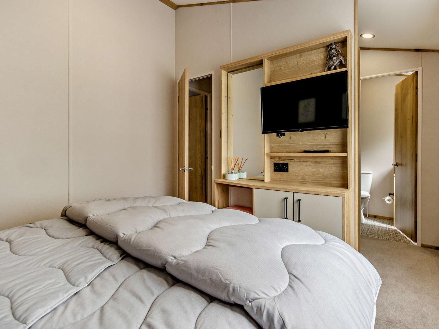 A bedroom with a bed, a TV mounted on a wooden wall, and a small desk with a chair.