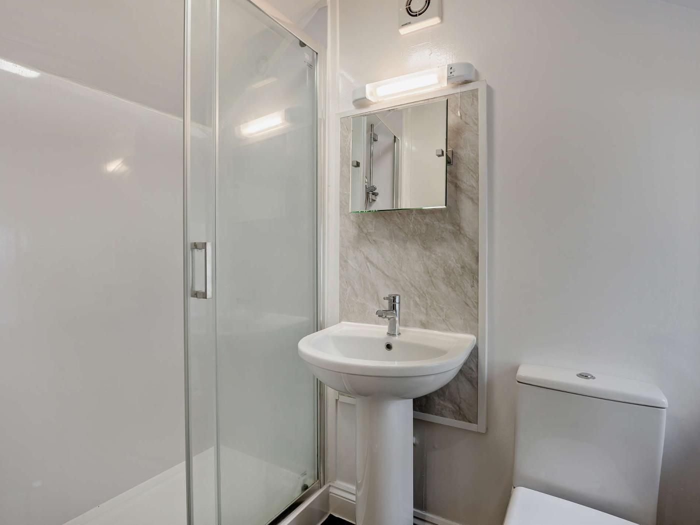 A modern bathroom with a glass shower enclosure, a pedestal sink, a toilet, and a wall-mounted mirror.