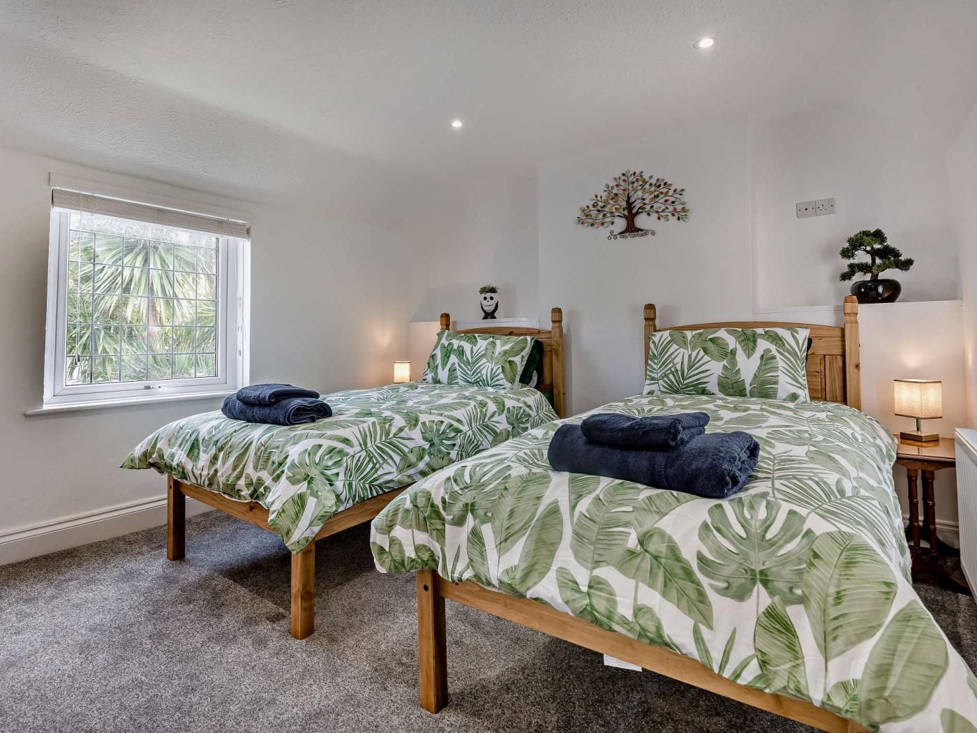 A bedroom with two single beds, a window, a wall-mounted tree decoration, and a bedside lamp.