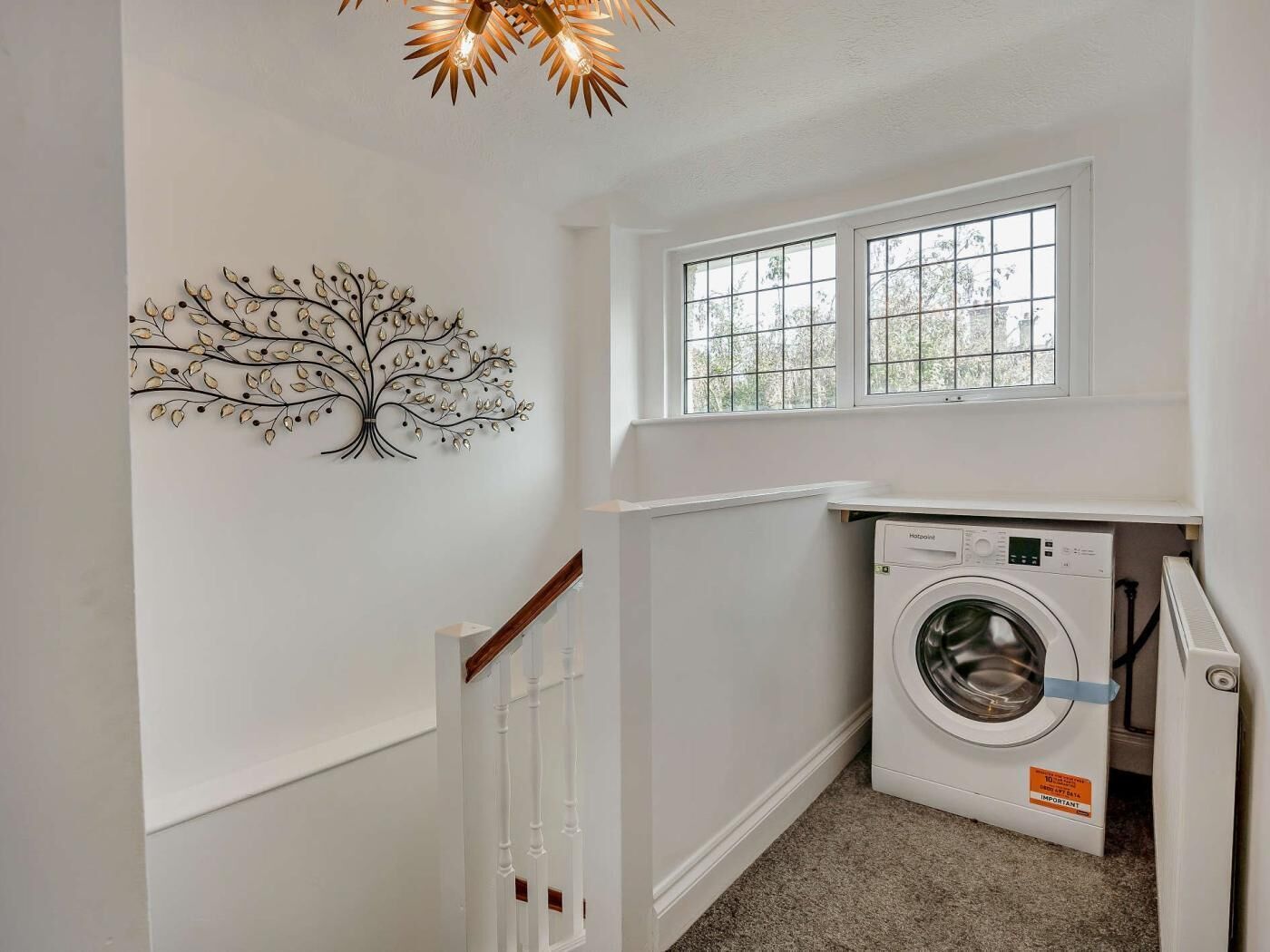 A laundry room with a wall-mounted washing machine, a window, and a tree-shaped wall decoration.