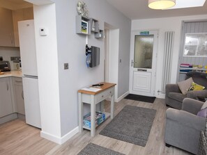 A compact living space with a kitchenette, a small table with a chair, a grey sofa, and a door with a frosted glass panel. - 1 Bed in Worthing (oc-80539) (Worthing)