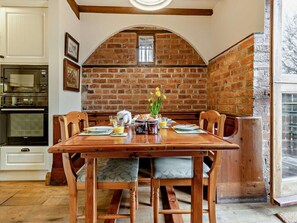 A dining area with a brick wall, wooden table, and chairs. - 2 Bed in Llanidloes (oc-94088) (Llanidloes)