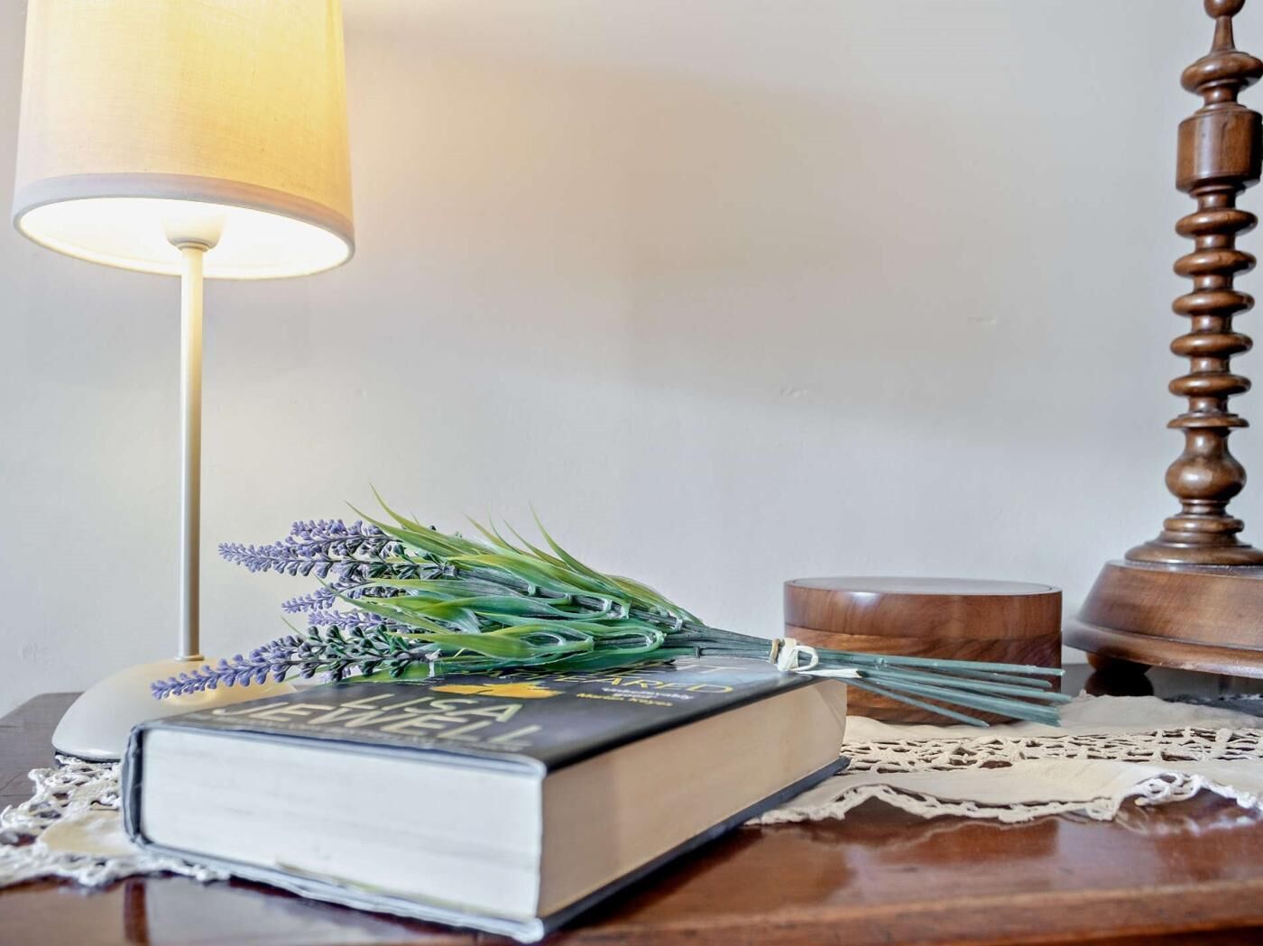 A book with a floral arrangement on a wooden table, a lamp, and a wooden object.