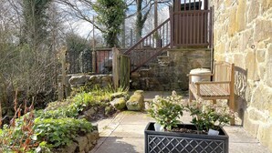 A stone building with a wooden staircase, a bench, and a planter box with plants. - 2 Bed in Llanidloes (oc-94088) (Llanidloes)