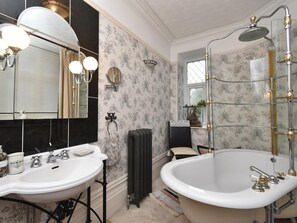 Ein Badezimmer mit zwei Waschbecken, einer großen Badewanne, einem Spiegel, einem Heizkörper und einem Fenster mit einer Pflanze.