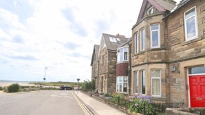 A row of stone houses with a red door, a clear road, and a beach in the background. - 4 Bed in Alnwick (oc-cn155) (Alnmouth)