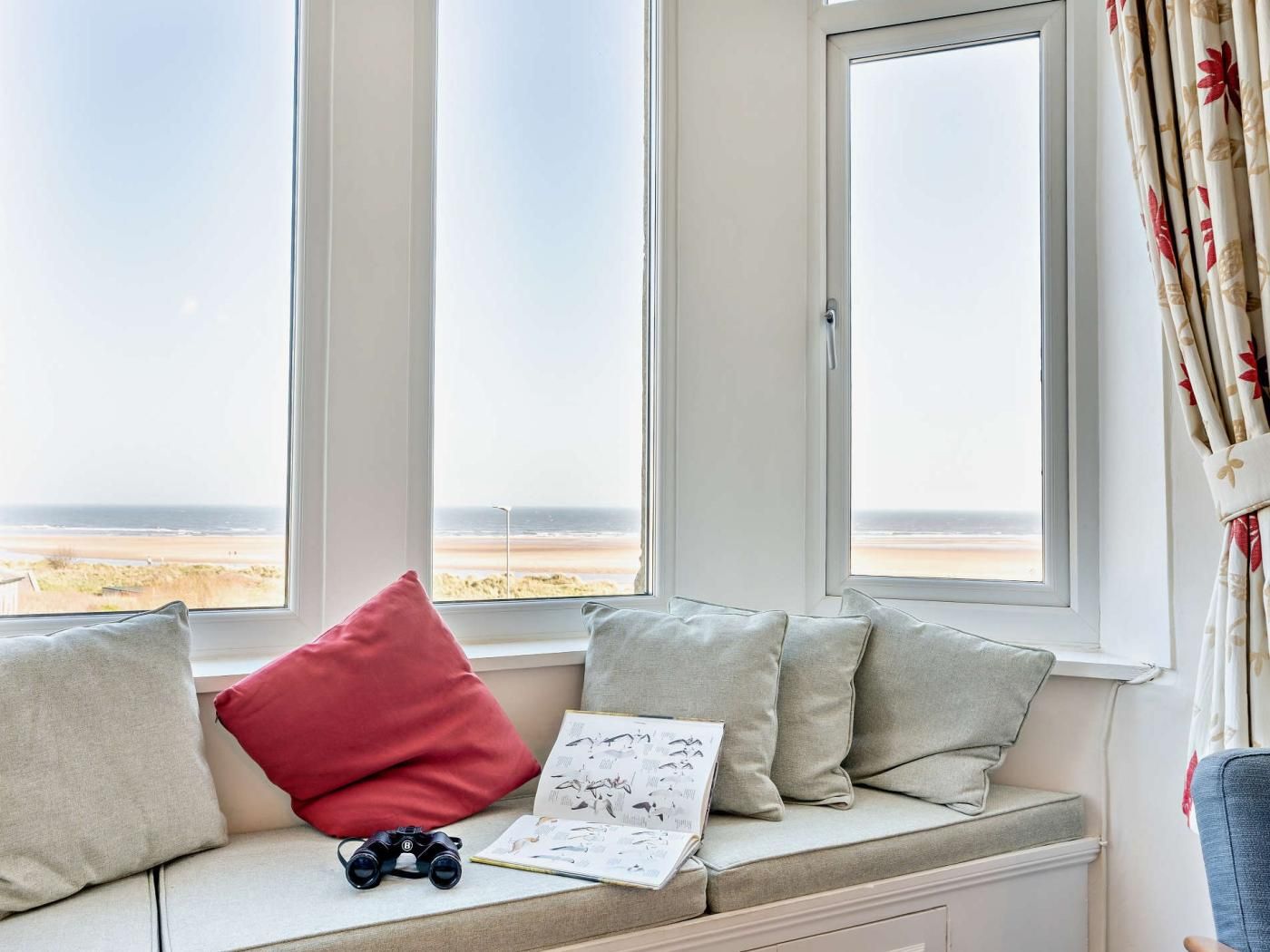 Et værelse med et vinduesbænk med udsigt over en strand, en bog og en kikkert.