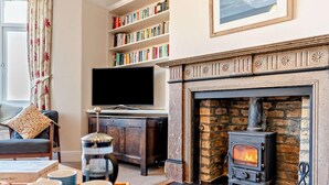 A cozy living room with a fireplace, bookshelves, a television, and a coffee table with mugs. - 4 Bed in Alnwick (oc-cn155) (Alnmouth)