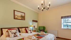Ein Schlafzimmer mit einem Bett, einem grünen Sessel, einem Fenster mit Blick und einer Chandelier.