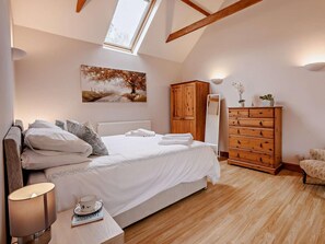 Een slaapkamer met een bed, een kaptafel, een spiegel, een lamp en een schilderij aan de muur.