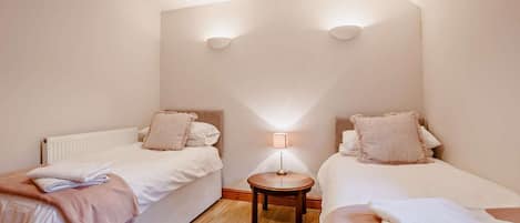 A bedroom with two single beds, a nightstand with a lamp, and a large window.