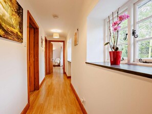 Ein Flur mit Holzboden, einem Fenster mit pinkfarbenen Blumen und einer Tür zu einem anderen Zimmer.