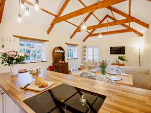 Eine geräumige Küche mit Holzboden, ein Essbereich mit weißen Stühlen und ein gemütliches Wohnzimmer mit einer Couch.