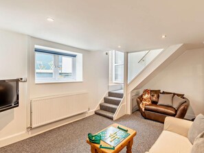 A modern living room with a flat-screen TV, a sofa, a coffee table with a board game, and a staircase leading to an upper floor. - 2 Bed in Cinderford (oc-93455) (Ruspidge and Soudley)