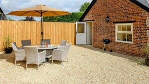 Een stenen huis met een terras van grind, een houten omheining en tuinmeubilair.